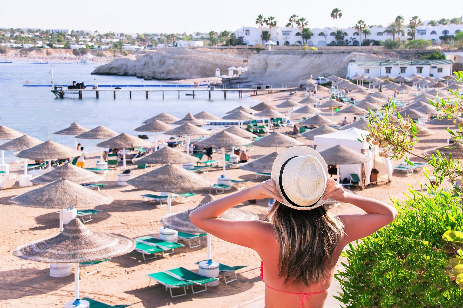 Kobieta w bikini i kapeluszu stoi przy plaży pełnej leżaków w Sharm el Sheikh w Egipcie