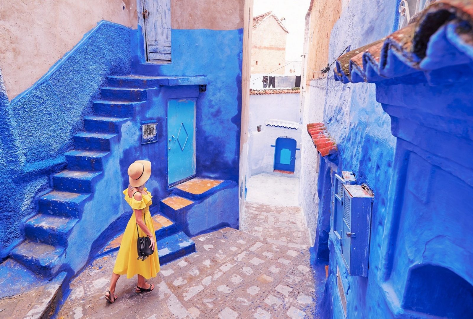 młoda kobieta w żółtej sukience spaceruje po medynie w niebieskim mieście Szafszawan w Maroko