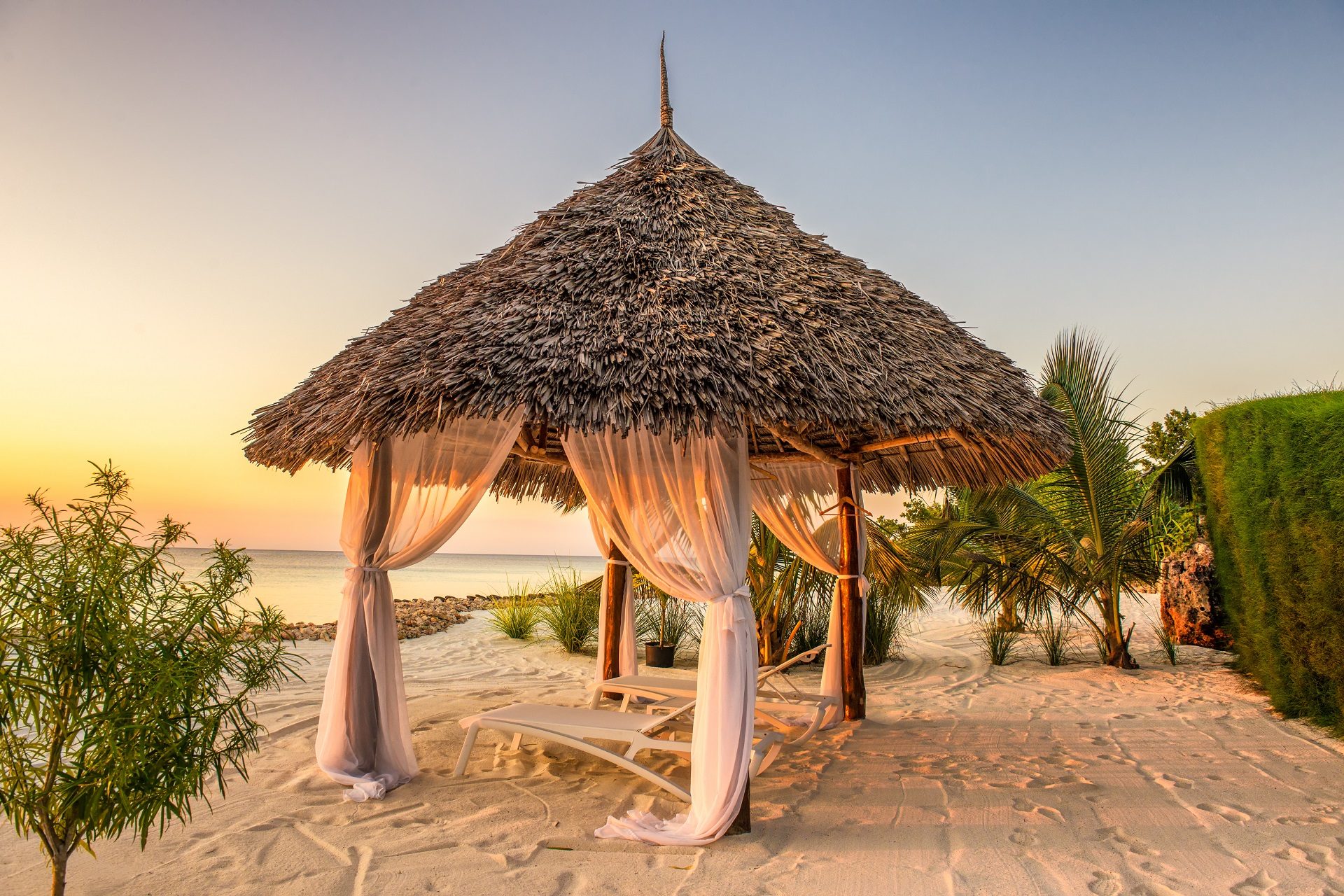 Łóżka balijskie na tle zachodzącego słońca na białej plaży na Zanzibarze w Tanzanii