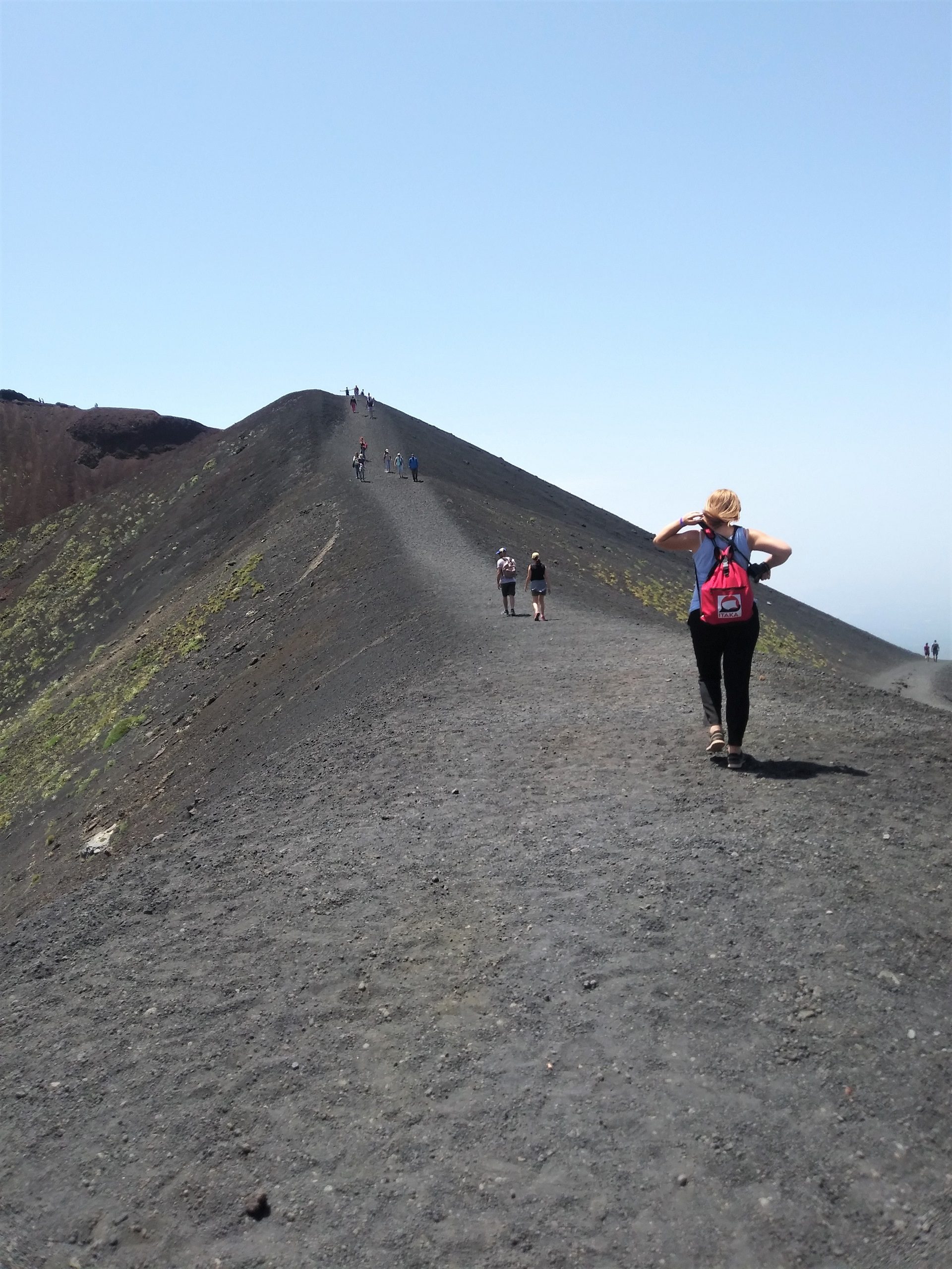 kobieta z czerwonym plecakiem wchodzi szlakiem wokół górnego krateru Silvestre na wulkanie Etna na Sycylii
